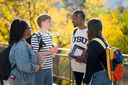 Four diverse students chatting outdoors with yellow trees background