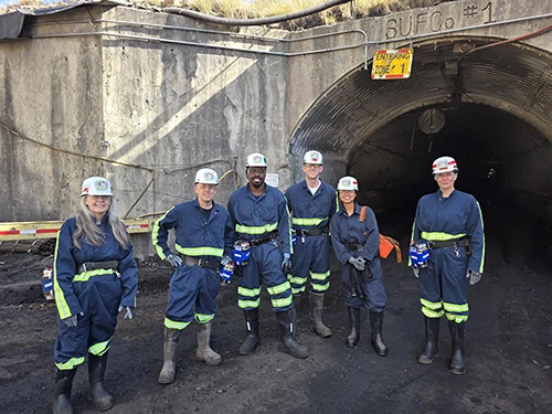 Six miners in safety gear standing before a tunnel entrance