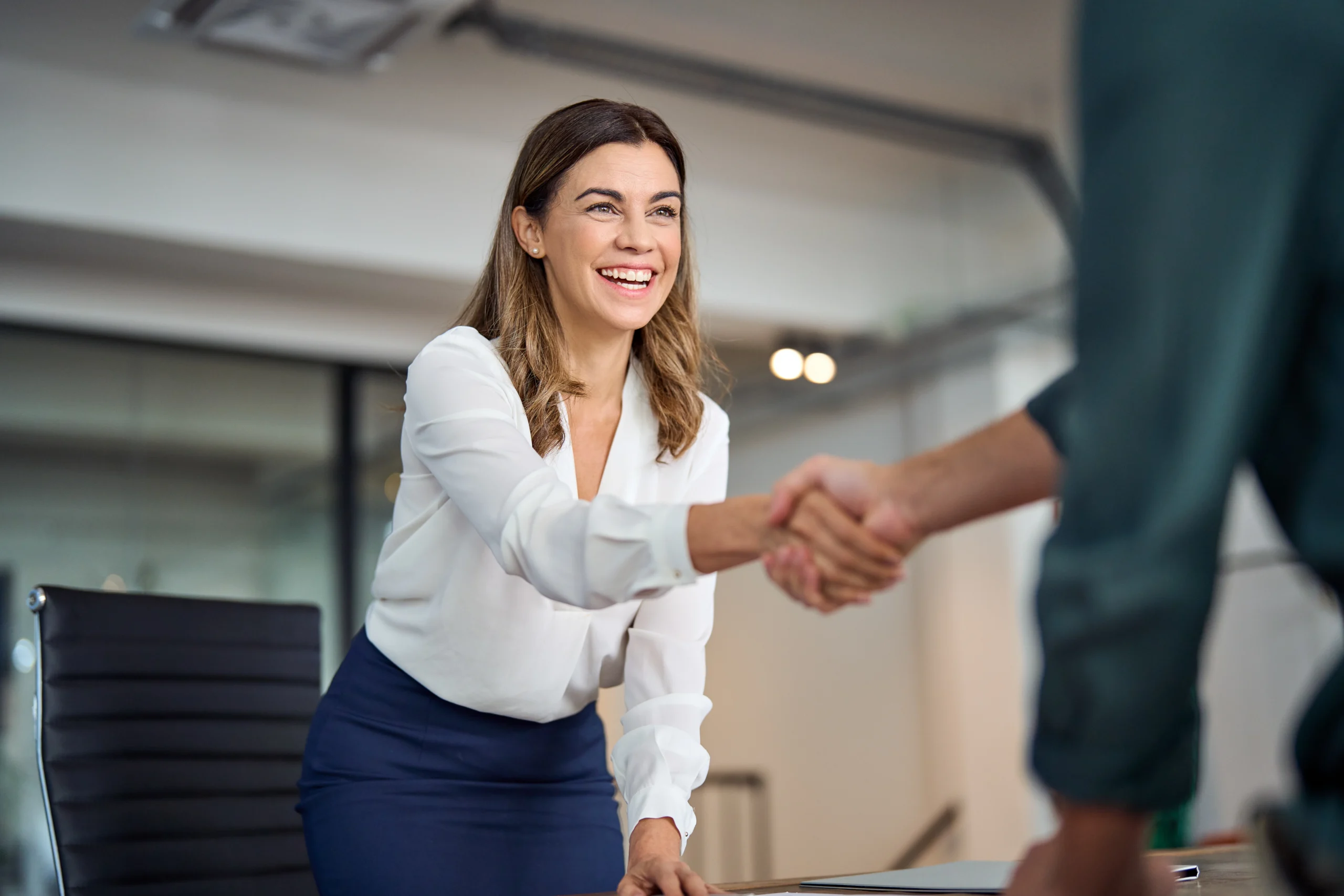 A happy businesswoman in an office shaking hands with another person